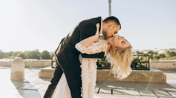 2024 Trending wedding styles and the shoes to match. Groom dipping his bride to kiss her on her neck in front of the Eiffel Tower on their wedding day.