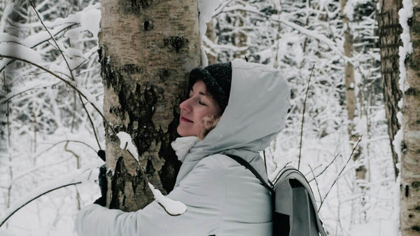 Woman in the snow hugging a tree and wearing a white rain coat and Rains Backpack. Our guide to Rains Backpacks: Your ultimate outdoor companion